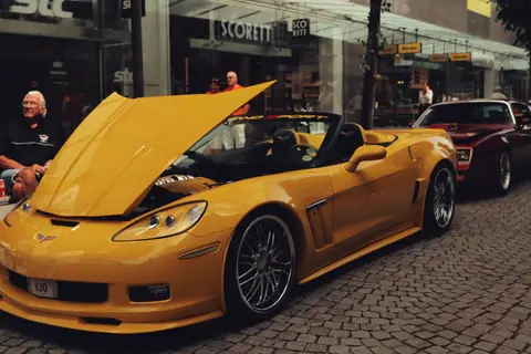 A yellow Chevrolet Corvette with an open hood on a cobblestone street in Jönköping, Sweden.