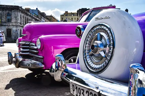 Close-up of classic pink cars in a Cuban town, showcasing vintage charm and urban culture.
