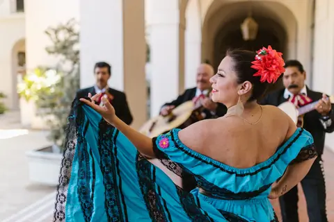 Mexican woman in blue dress dancing with mariachi band in background.