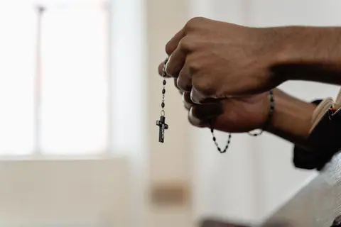 Hands holding a rosary, symbolizing faith and prayer in a religious setting.