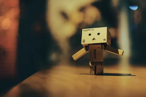Cardboard toy robot standing on a wooden surface with warm bokeh lights in the background.
