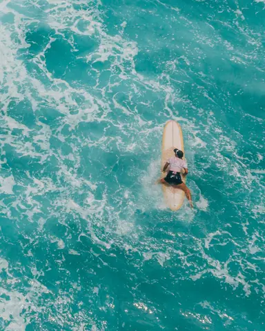 High-angle view of a surfer enjoying the summer waves on a vibrant turquoise sea.