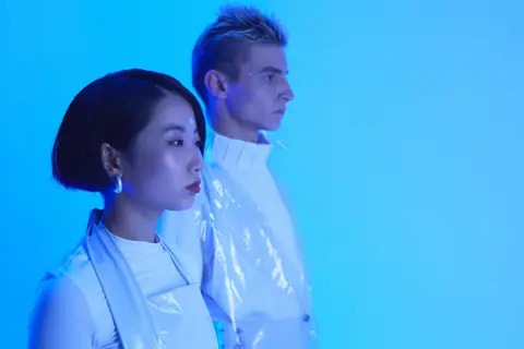 Futuristic fashion portrait of an Asian woman and Caucasian man in blue lighting, showcasing minimalist style.