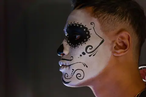Close-up side view of a man with intricate Dia de los Muertos face paint.