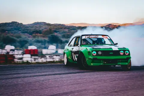 Green sports car drifts on a race track in Sparti, showcasing speed and action.