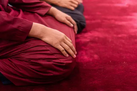 Muslim man in traditional attire praying indoors on a red carpet, focusing on spirituality and tradition.