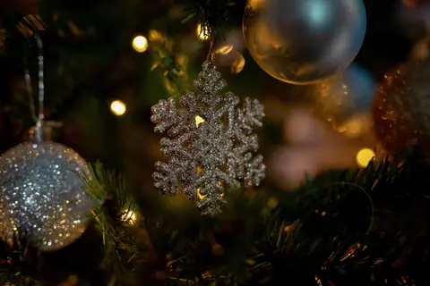 Close-up of a sparkling snowflake ornament on a decorated Christmas tree with lights.