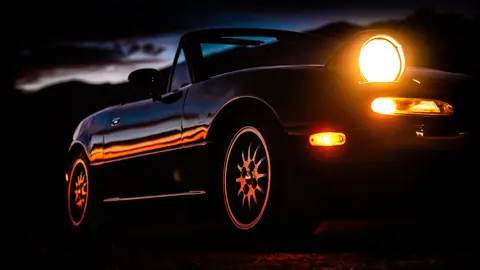 A sleek convertible sports car with headlights on, captured at sunset.