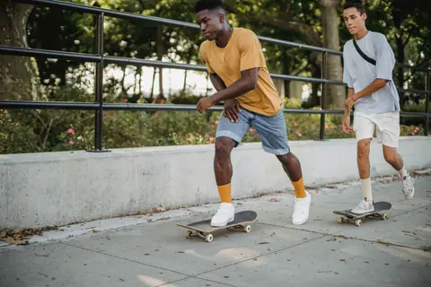Confident African American male wearing yellow t shirt riding skateboard while spending time together with friend on summer day in city street