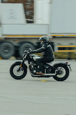 A biker in leather gear rides a vintage motorcycle on an open road.