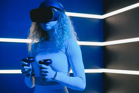 A woman using a VR headset and controllers in a futuristic blue-lit room.
