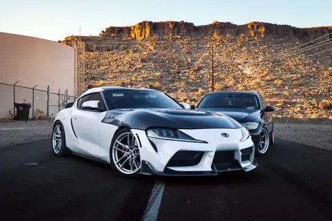 Two Toyota Supra sports cars parked on a deserted road with rocky desert background.