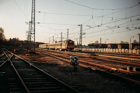 A train travels on railway tracks surrounded by infrastructure and power lines during sunset.