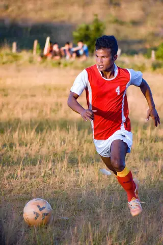 Focused soccer player in red uniform running towards the ball during daylight.