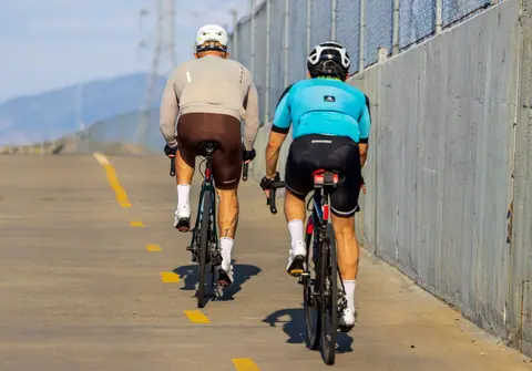 Two male cyclists wearing helmets and gear riding on an urban road during the day.