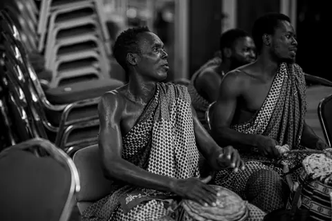 Men in traditional attire drumming at a cultural event in Accra, Ghana.