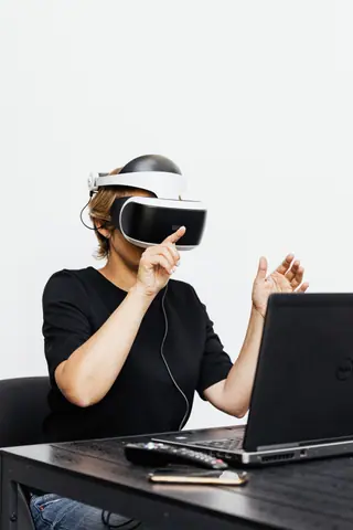 A woman using a VR headset interacts with a laptop, symbolizing futuristic technology.