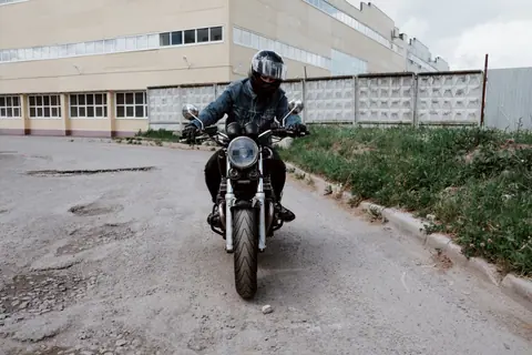 A person wearing a denim jacket rides a motorcycle in an urban setting, showcasing adventure and style.