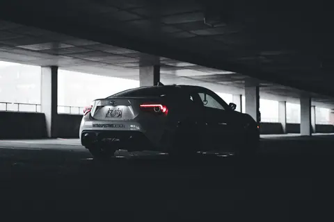 A stylish sports car with illuminated taillights parked in a dimly lit urban garage, showcasing modern design aesthetics.
