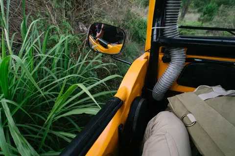 Crop unrecognizable male traveler in casual clothes sitting in front seat of modern truck car and taking selfie in rear viewer while riding in lush green rural hillside