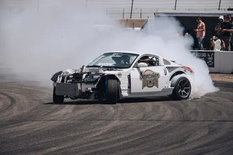 High-speed drift racing car in action with white livery and billowing smoke on a racetrack.