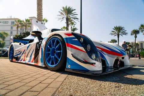Dynamic shot of a sleek racing car outdoors, featuring striking red, white, and blue design under palm trees.