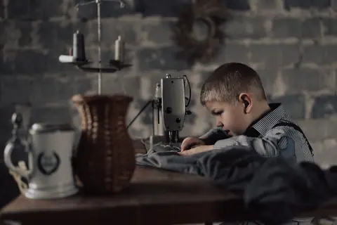A young boy intently sewing with a machine in a workshop setting, showcasing concentration and skill.