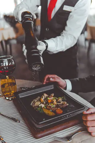 Elegant gourmet meal being served by a waiter in a high-end restaurant setting, adding pepper.