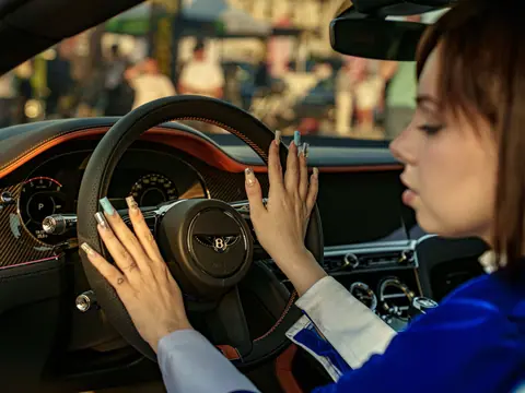 Young woman touching steering wheel of luxury car interior, depicting elegance and sophistication.