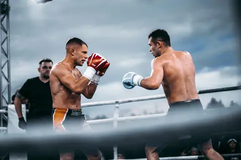 Two male boxers engaging in a competitive outdoor match, displaying strength and skill in the ring.