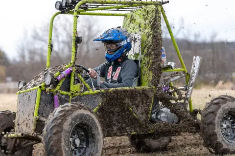 Off-road kart speeding through a muddy field, showcasing thrilling motorsport action.