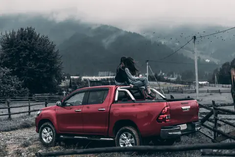 Two women sitting on a red pickup truck surrounded by foggy mountain landscape, capturing the essence of adventure and friendship.
