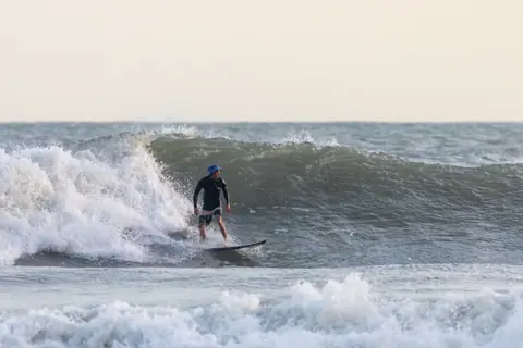 An adult male surfer expertly rides a wave in open ocean waters, showcasing surfing skills.