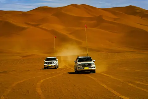 Two SUVs traverse vast desert dunes, capturing the thrill of off-road travel.