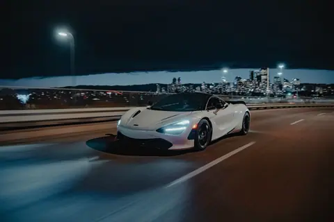 A sleek white sports car drives on a highway with the Calgary skyline illuminated in the background.