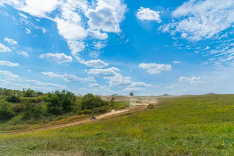 A dirt biker navigates a rugged path through lush green hills under a bright blue sky. Perfect outdoor adventure.