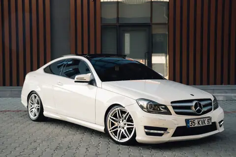 A polished white Mercedes-Benz coupe parked in front of a modern building facade.
