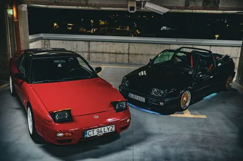 Two classic sports cars in a dimly lit parking garage at night, creating a dramatic urban scene.