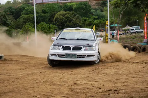 A rally car kicks up dust while drifting on a dirt track during a racing event.
