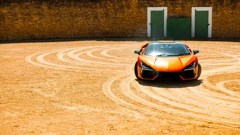 Orange sports car doing donuts in open arena with stone walls.