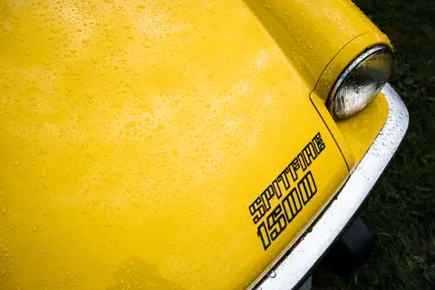Detailed view of a yellow Triumph Spitfire 1500 hood with water droplets.