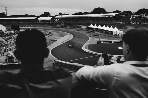 Spectators watch a thrilling motorsport race from the stands in black and white.
