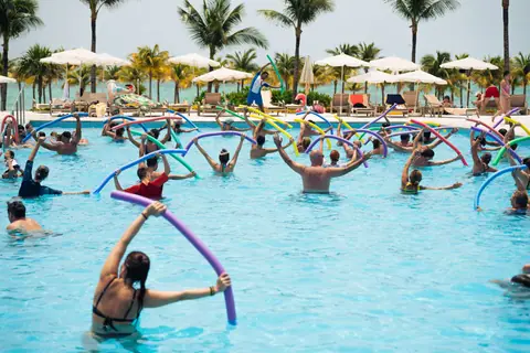 Group enjoying aqua aerobics with noodles by the pool in a tropical Cancún resort, Mexico.