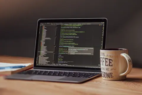 Laptop displaying code editor with coffee mug on desk, perfect for tech themes.