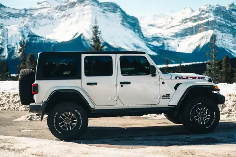 White Jeep Wrangler parked with scenic snowy mountain backdrop in Jasper, Alberta.
