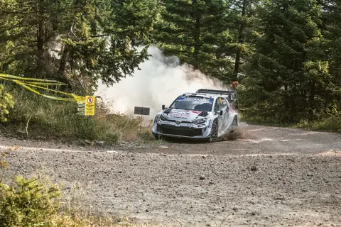 A rally car speeds through a dusty forest track in Pavliani, Greece during a thrilling race.