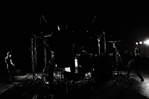 Dramatic black and white backstage view of a band performing live on stage.