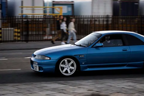 A sleek blue sports car speeds through city streets, capturing urban life in motion.