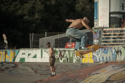 A young skateboarder executes a trick at an outdoor graffiti-covered skate park during the day.