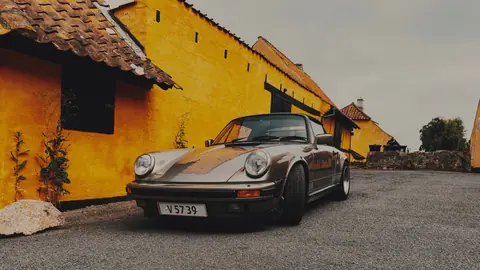 Vintage sports car parked by bright yellow rustic buildings in Denmark, scenic village view.